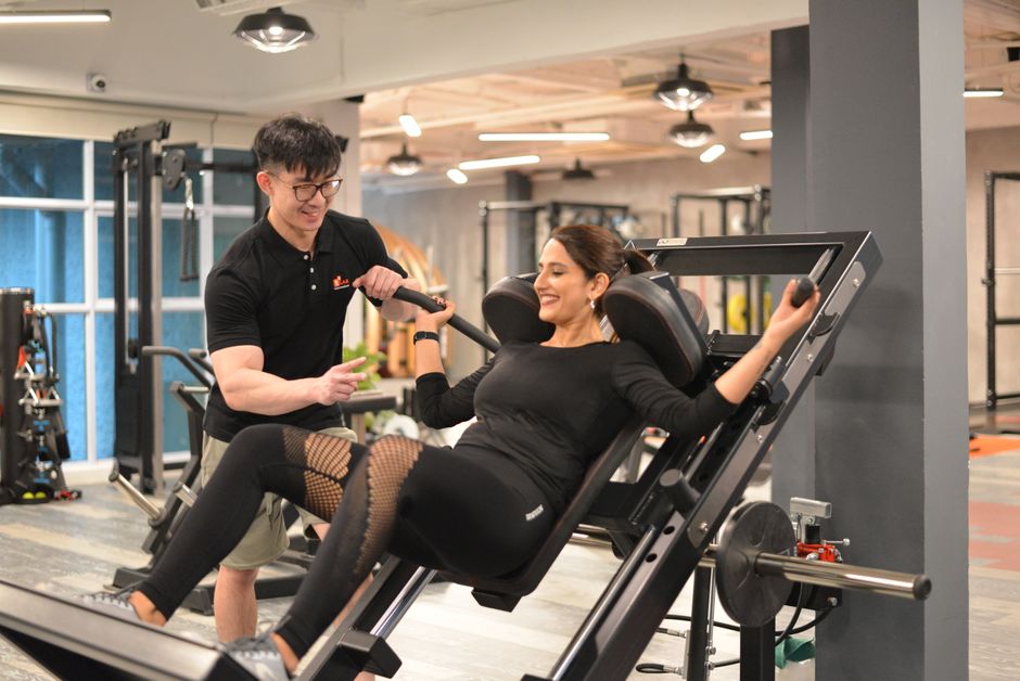 Trainerin unterstuetzt eine Frau beim Beintraining im Fitnessstudio