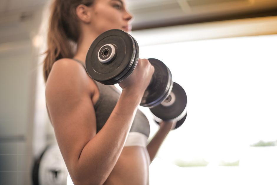 Frau trainiert konzentriert mit Kurzhanteln im Fitnessstudio