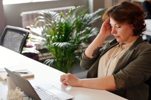 Frau haelt sich gestresst den Nacken am Schreibtisch im Homeoffice