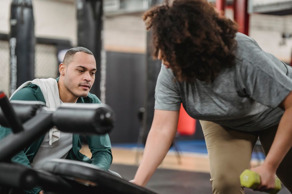 Trainer begleitet eine Kundin engmaschig beim Krafttraining mit Kurzhanteln