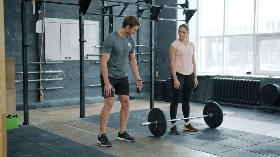 Trainer erklärt einer Frau die Technik beim Training mit der Langhantel